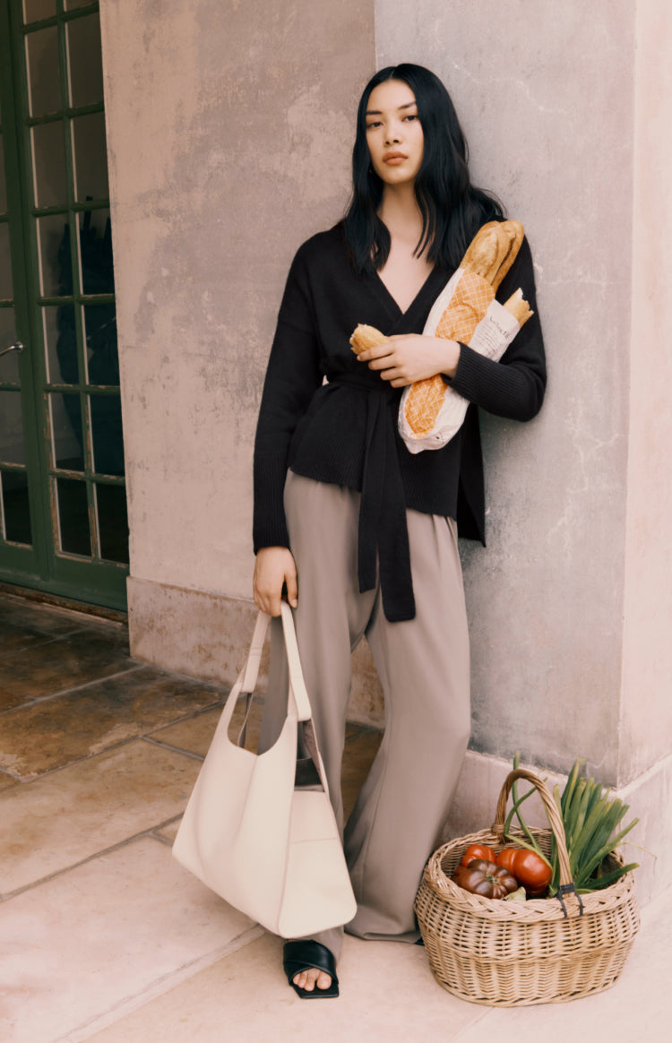 Woman standing by door with a tote bag, bread, and basket of groceries.