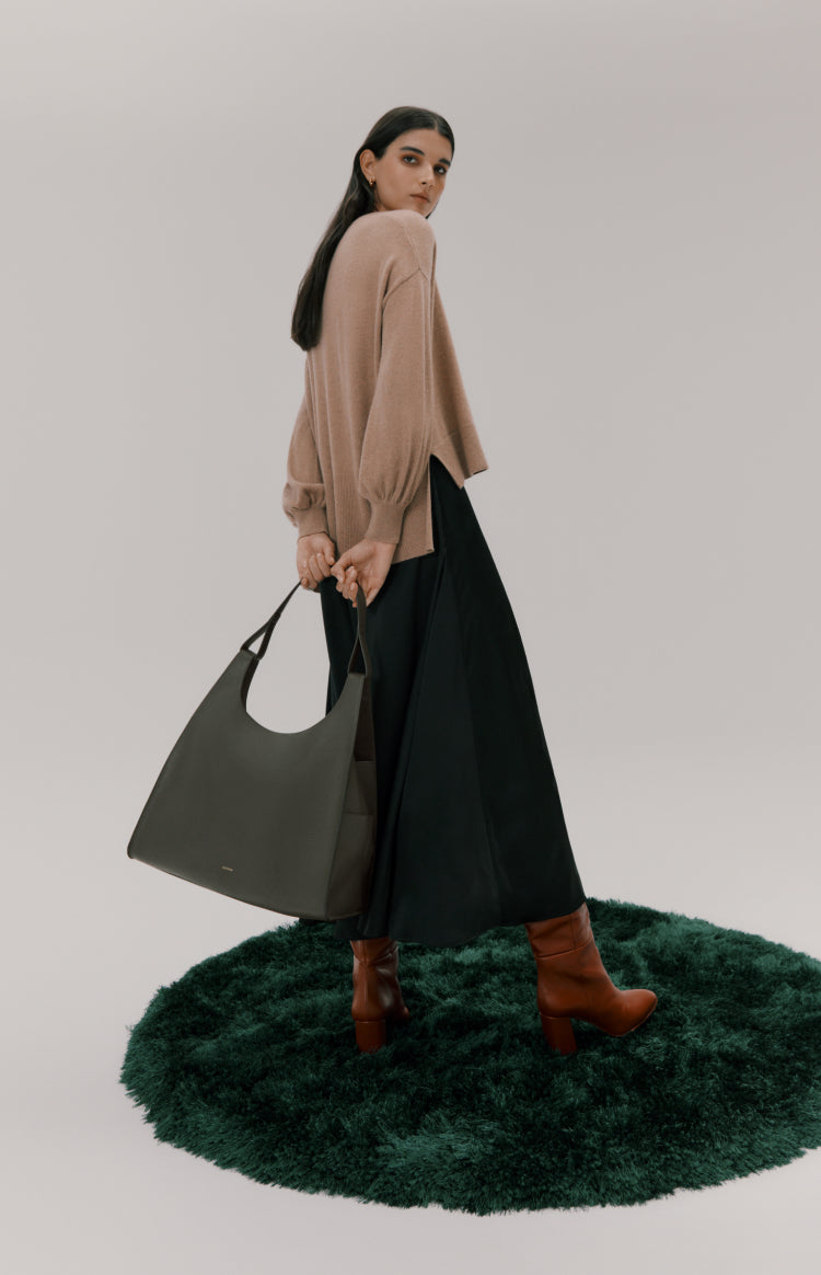 Woman walking carrying a large bag, looking over her shoulder.