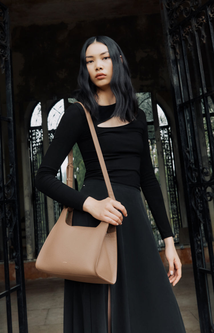 Woman in a dress holding a handbag standing near a gate.