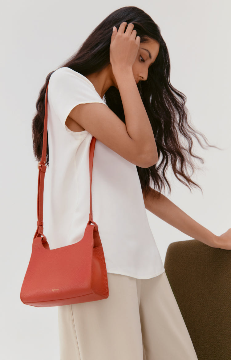 Woman standing and touching her hair while carrying a shoulder bag.