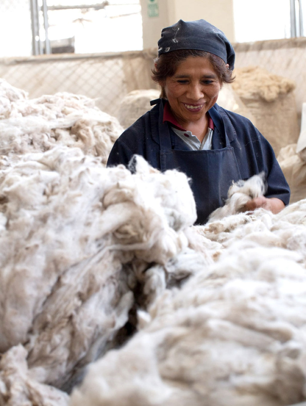 Woman smiling while working with large piles of wool.