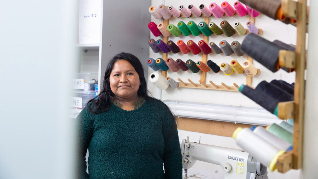 Woman standing in a sewing workshop with thread spools and equipment in the background.