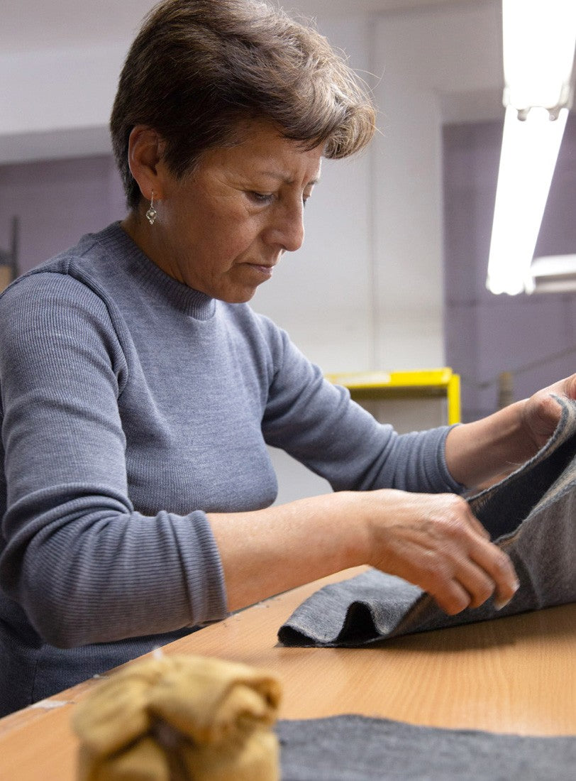Woman sewing fabric at a table in a workshop.