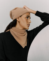 Woman wearing a beanie and sweater, holding her head, looking away.
