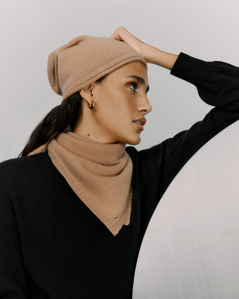 Woman in a beanie and turtleneck holding her hat looking to the side.