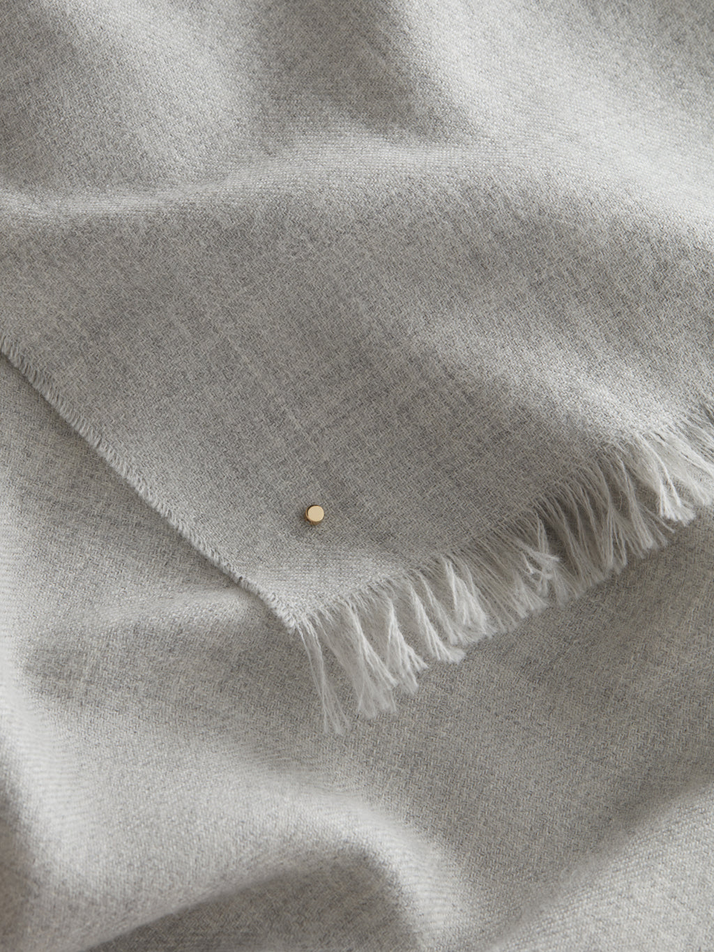 Fabric with a small button and fringed edge folded on itself.