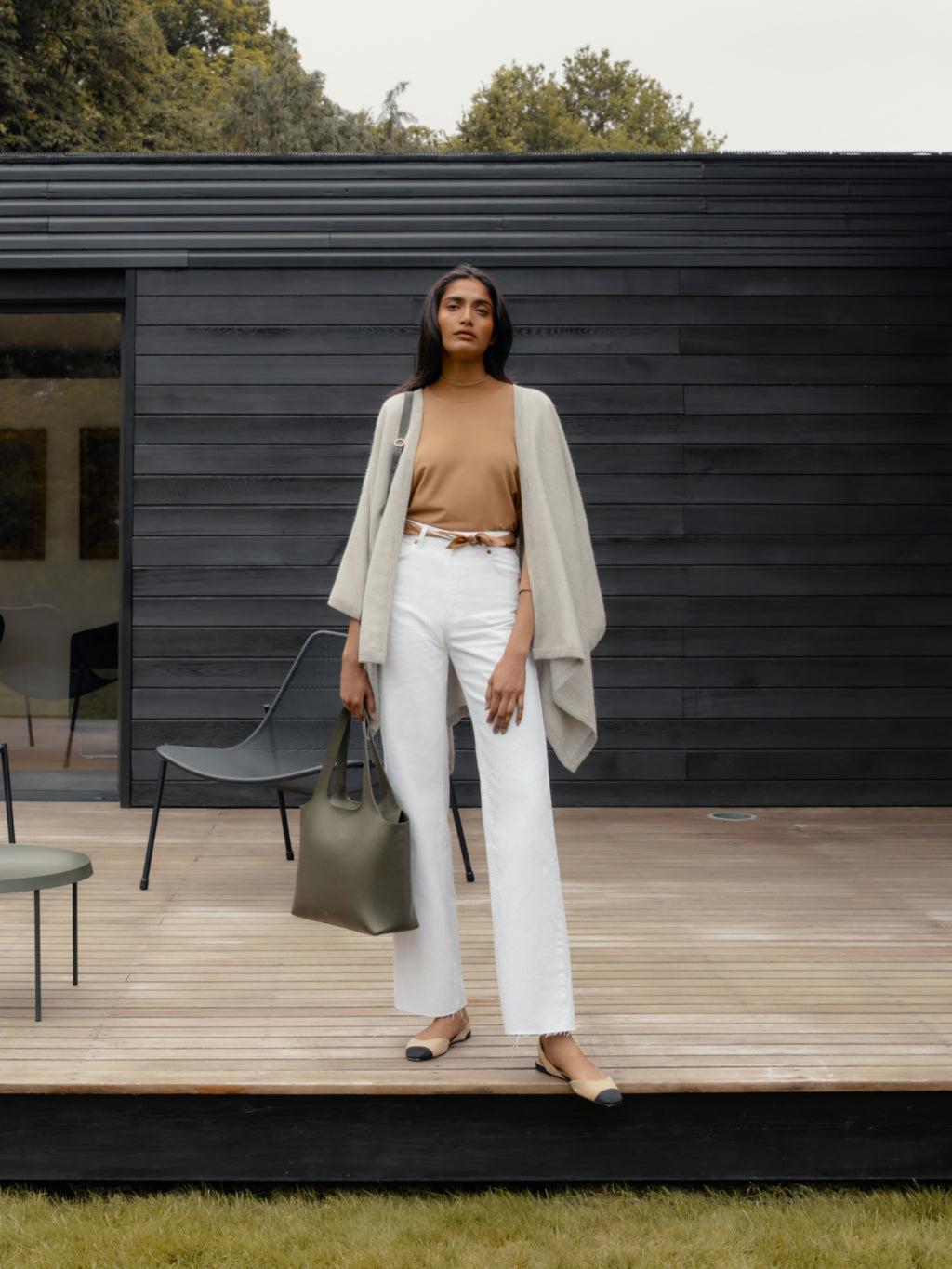 Woman standing on a wooden deck with a handbag, looking at the camera.