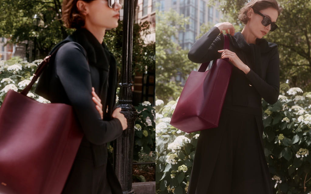 Woman holding large tote bag outdoors with greenery in the background