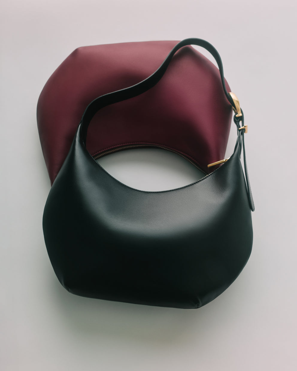 Two crescent-shaped shoulder bags overlapping on a flat surface