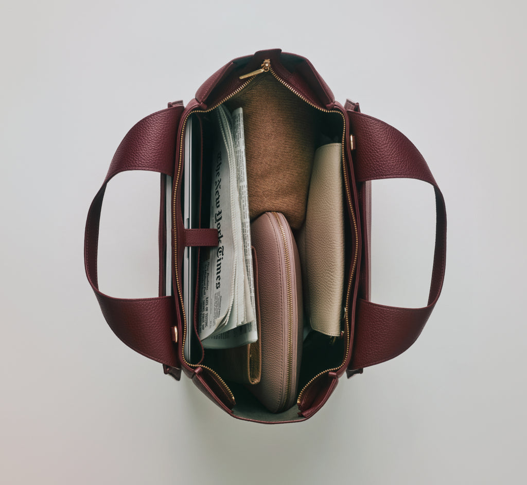Open handbag containing a newspaper and two pouches.