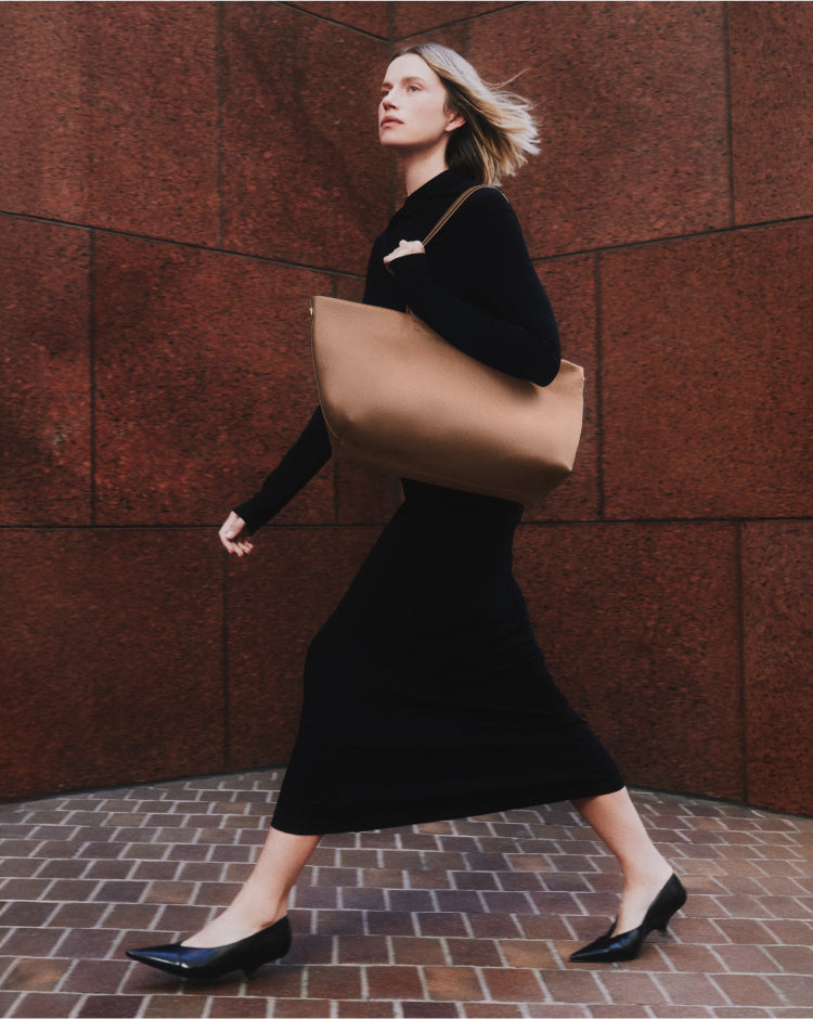 Person walking with large handbag wearing long dress and flat shoes.