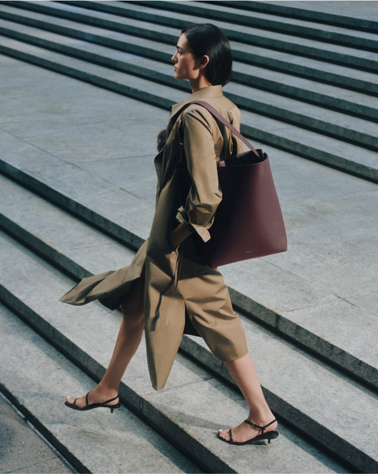Person in a long coat walking up steps carrying a large shoulder bag.