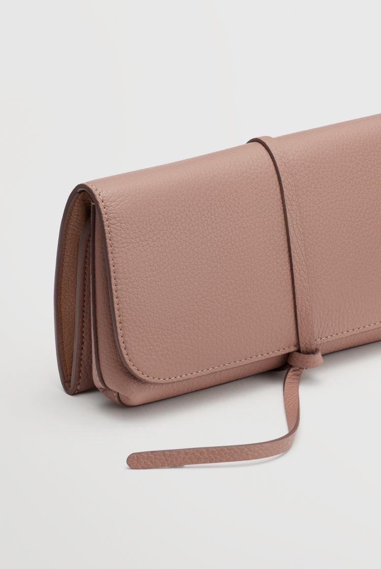 Rolled clutch purse with wraparound strap on a plain background.