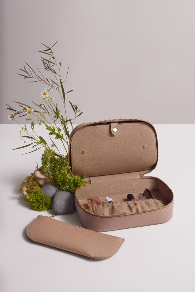 Open jewelry box with compartments next to floral arrangement and a small pouch.