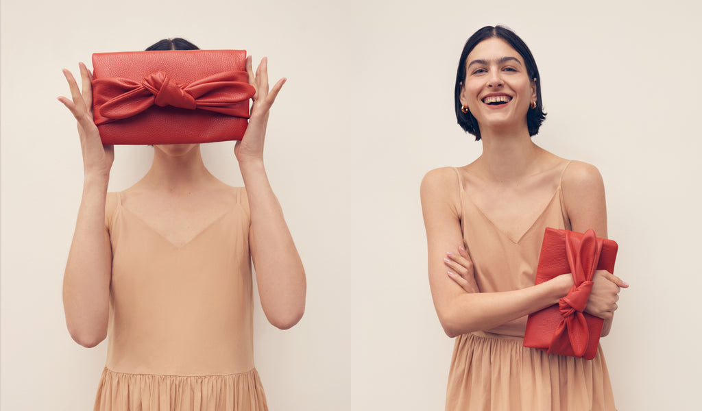 Woman holding gift in front of her face and smiling holding a clutch.