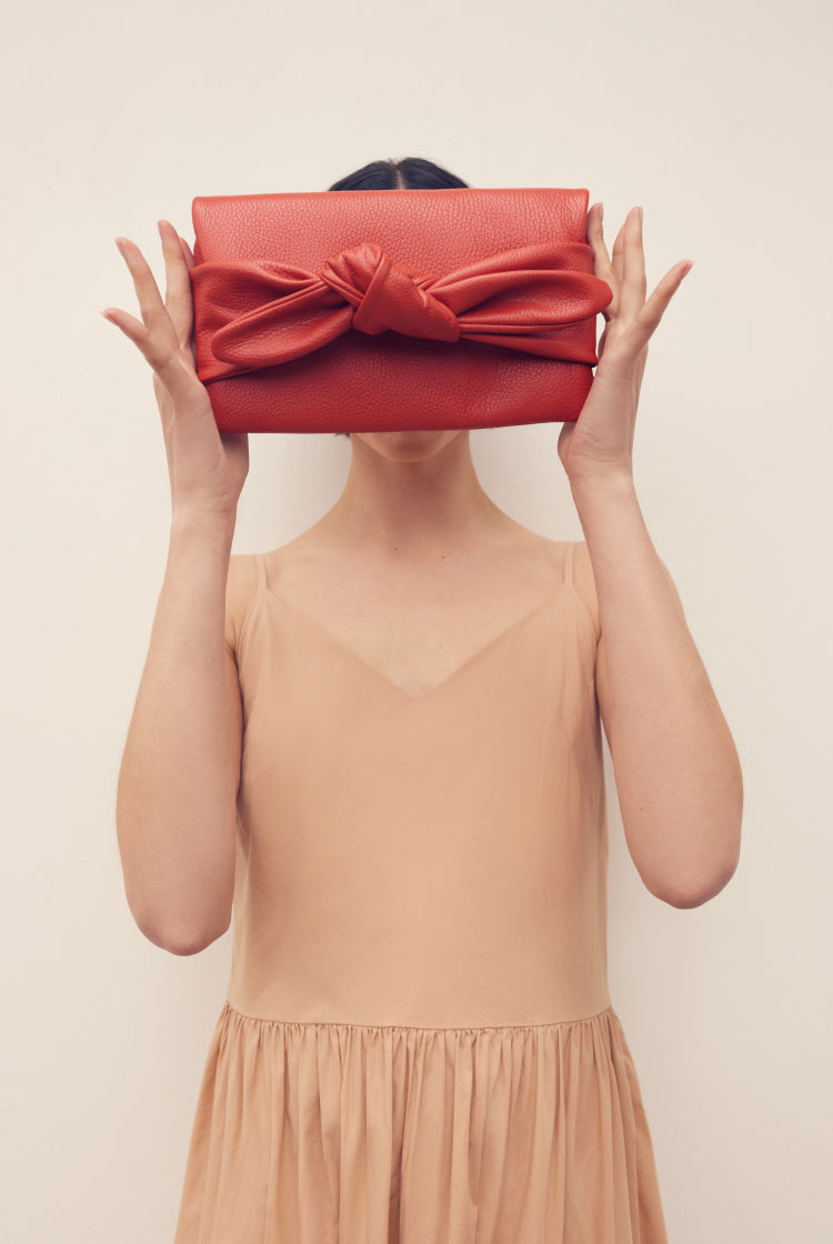 Person holding a clutch with a bow over their face.