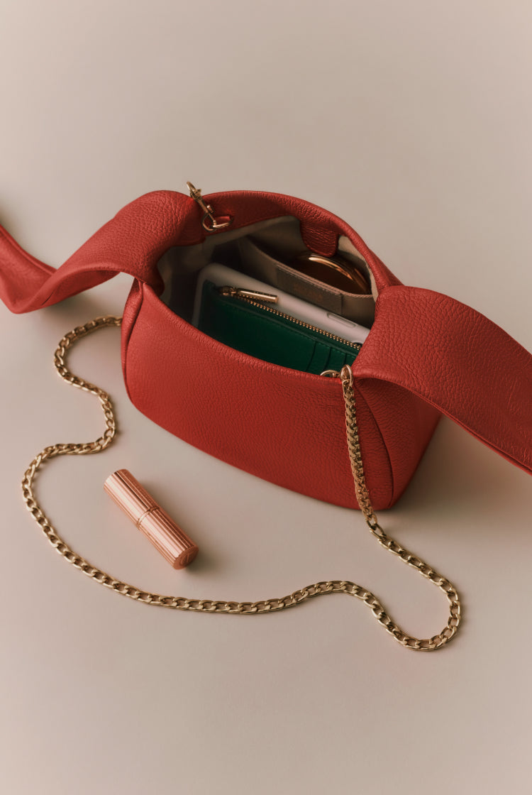 Open handbag with items inside and a chain strap beside it.