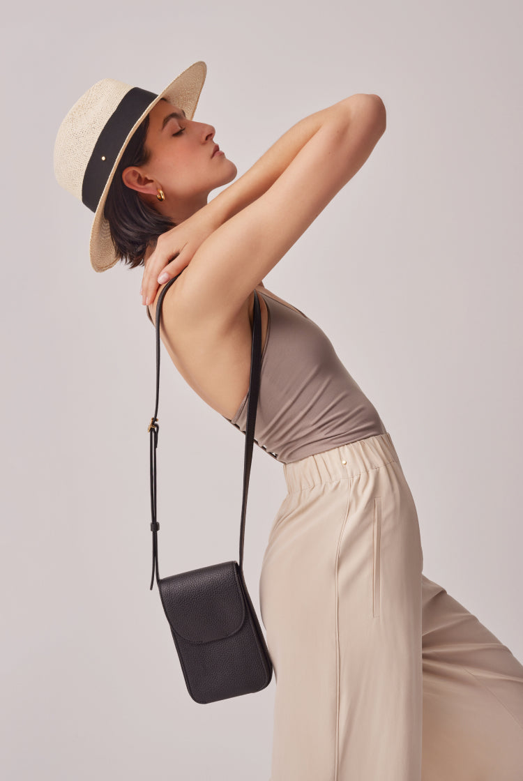 Woman posing with hat and bag, eyes closed and arm on neck.