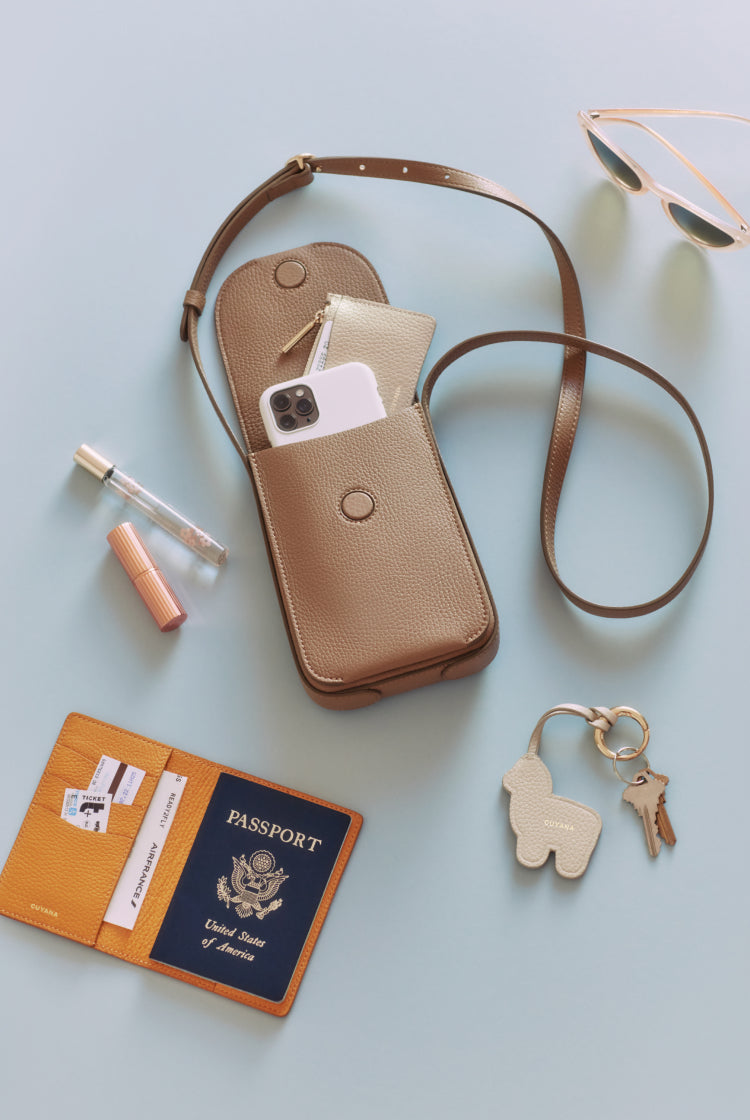 Purse with strap, sunglasses, passport, keys, and cosmetic products arranged on a surface.