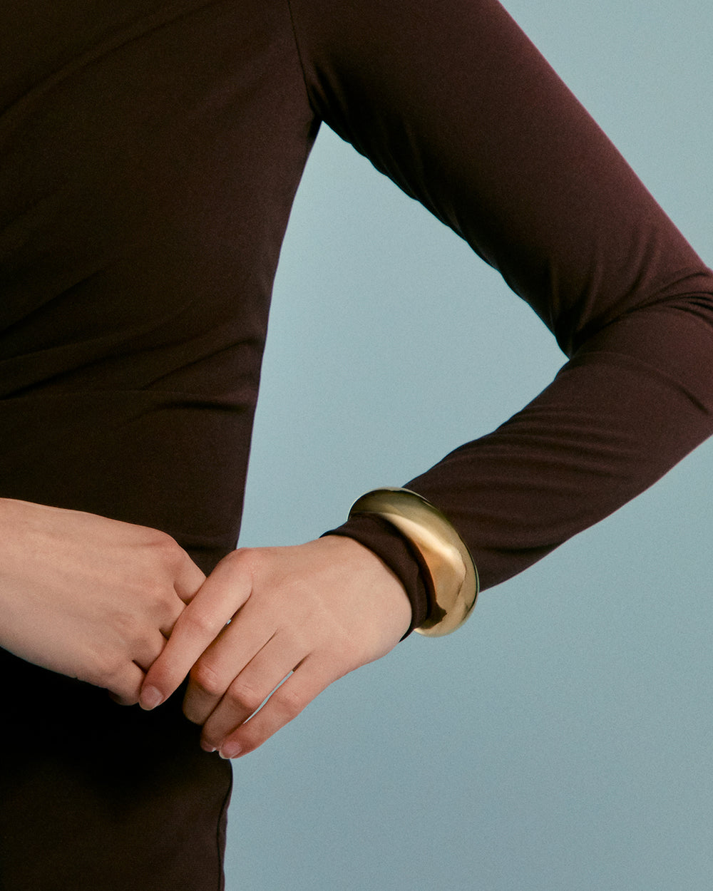 Person wearing a long sleeve shirt and a bracelet, hands clasped.