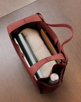 Open tote bag with items like a notebook, rolled fabric, pen, and bottle inside.