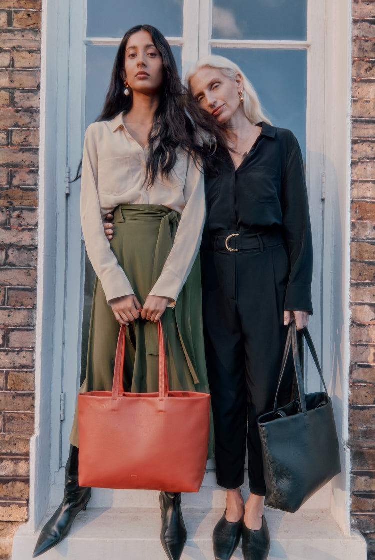 Two women standing by a door, each holding a handbag.