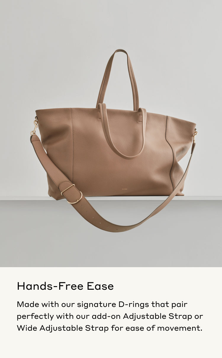 Handbag with dual handles and an adjustable shoulder strap, floating against a plain backdrop.
