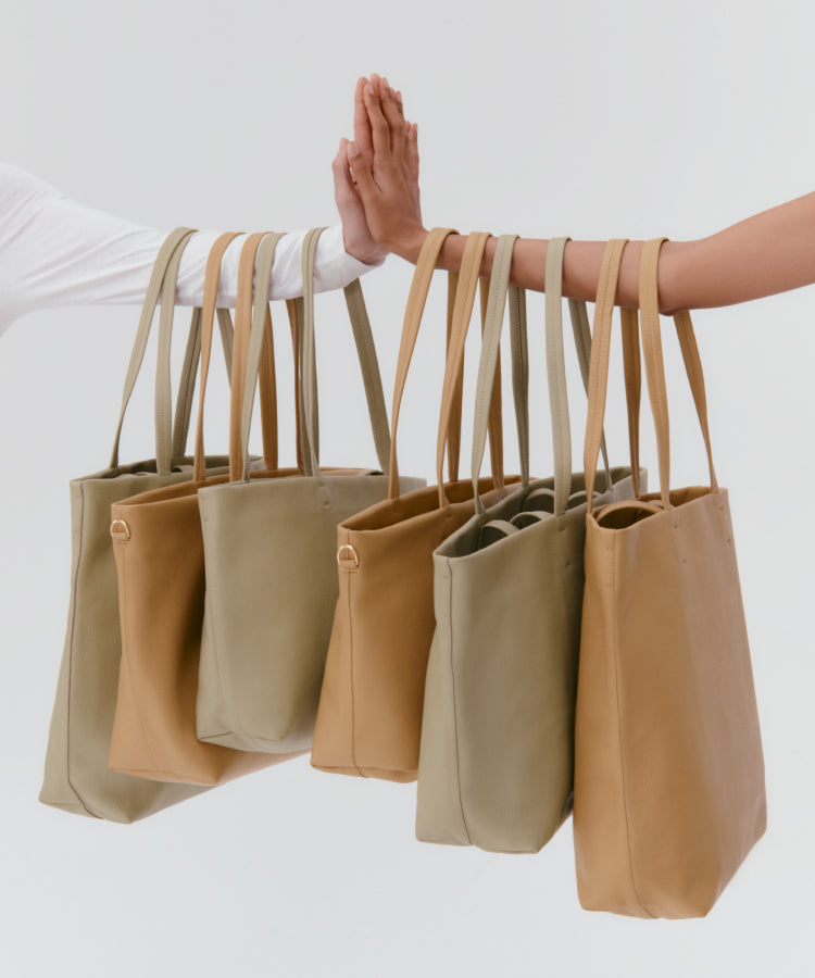 Two hands holding multiple tote bags by the straps.