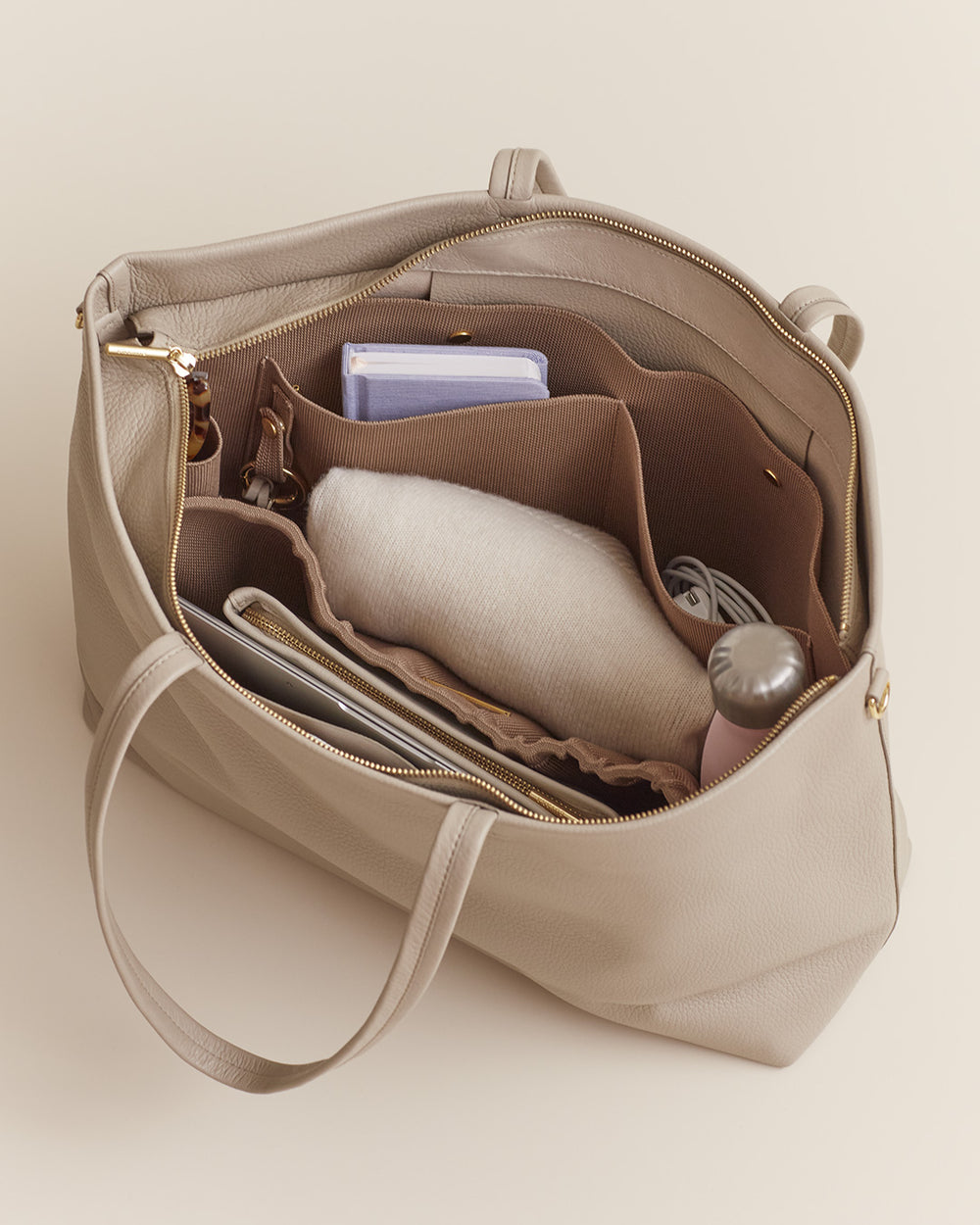 Open handbag with various items inside like a scarf, notebook, and sunglasses.