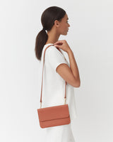 Woman standing sideways with a shoulder bag.