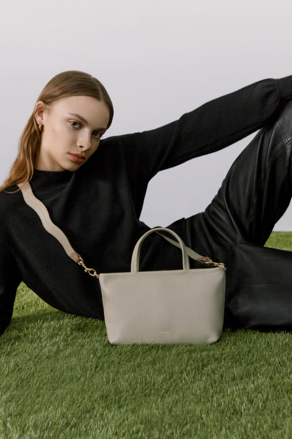 Woman reclining on grass with a handbag next to her.