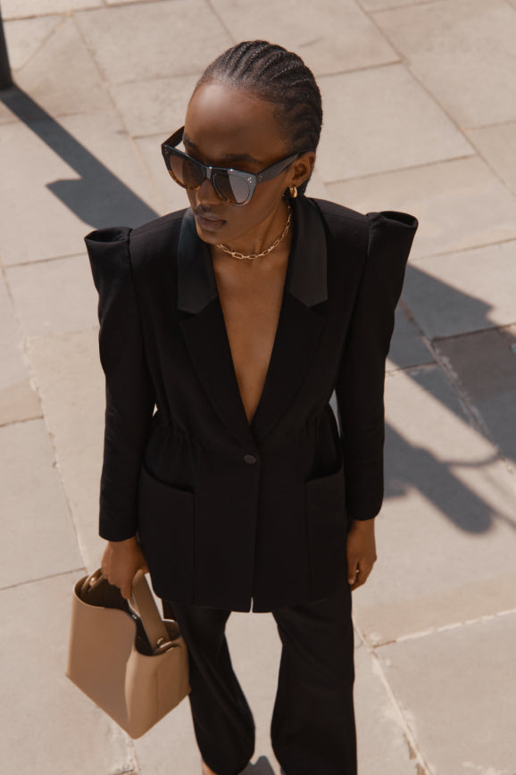 Woman in business attire and sunglasses walking outdoors.