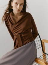 Woman sitting on a chair, wearing a wrapped top and skirt.