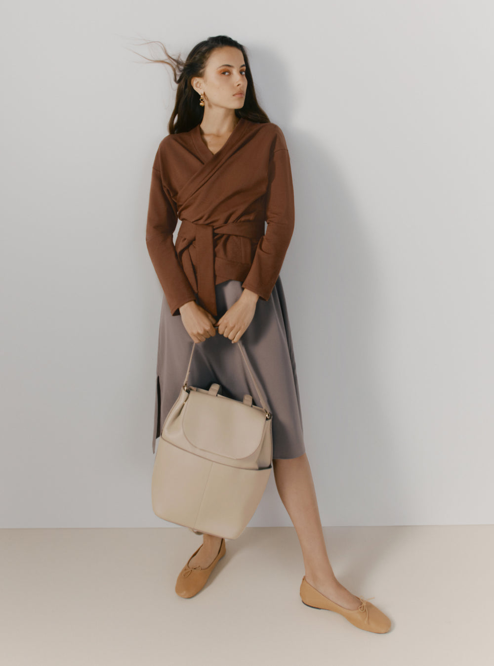Woman in a wrap top and skirt holding a handbag and looking away.