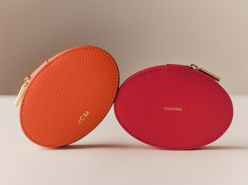 Two oval leather pouches with zippers on a table.