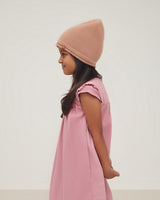 Young girl wearing a beanie and dress, profile view.