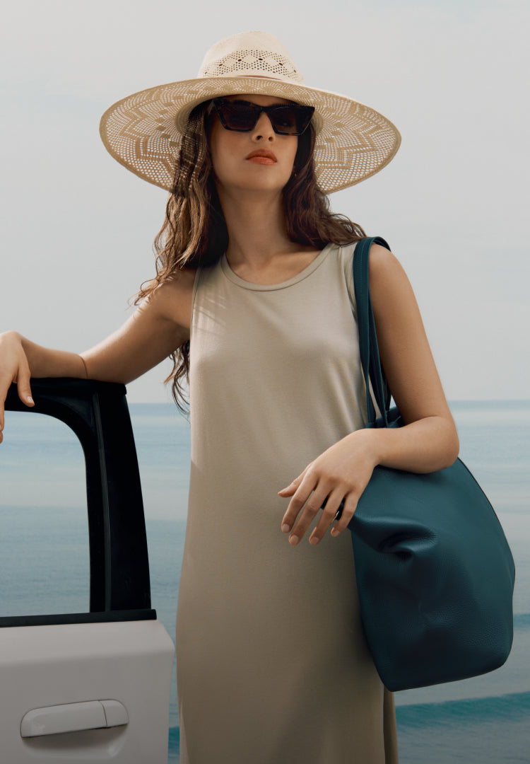 Model wears straw hat, large green tote and light green dress. 