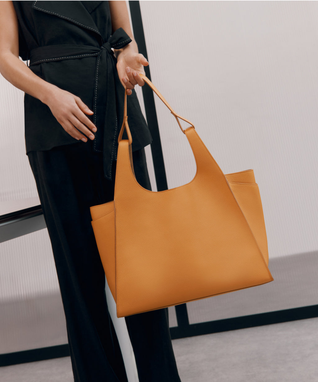 Model in Black carries large tote in color orange. Linked image.