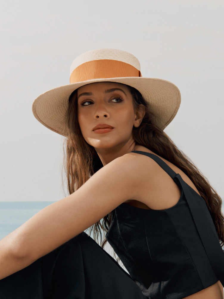 Person sitting by the sea wearing a sun hat and sleeveless top.