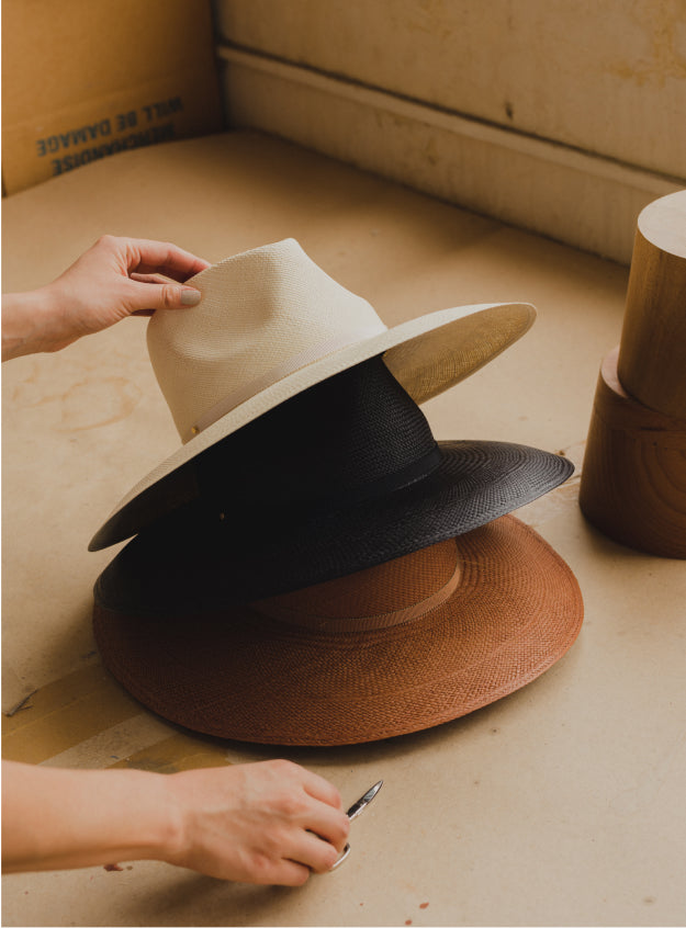 Three stacked hats with a hand adjusting the top one near a wooden object.