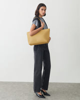 Person holding a shoulder bag, wearing a shirt, pants, and pointed shoes.