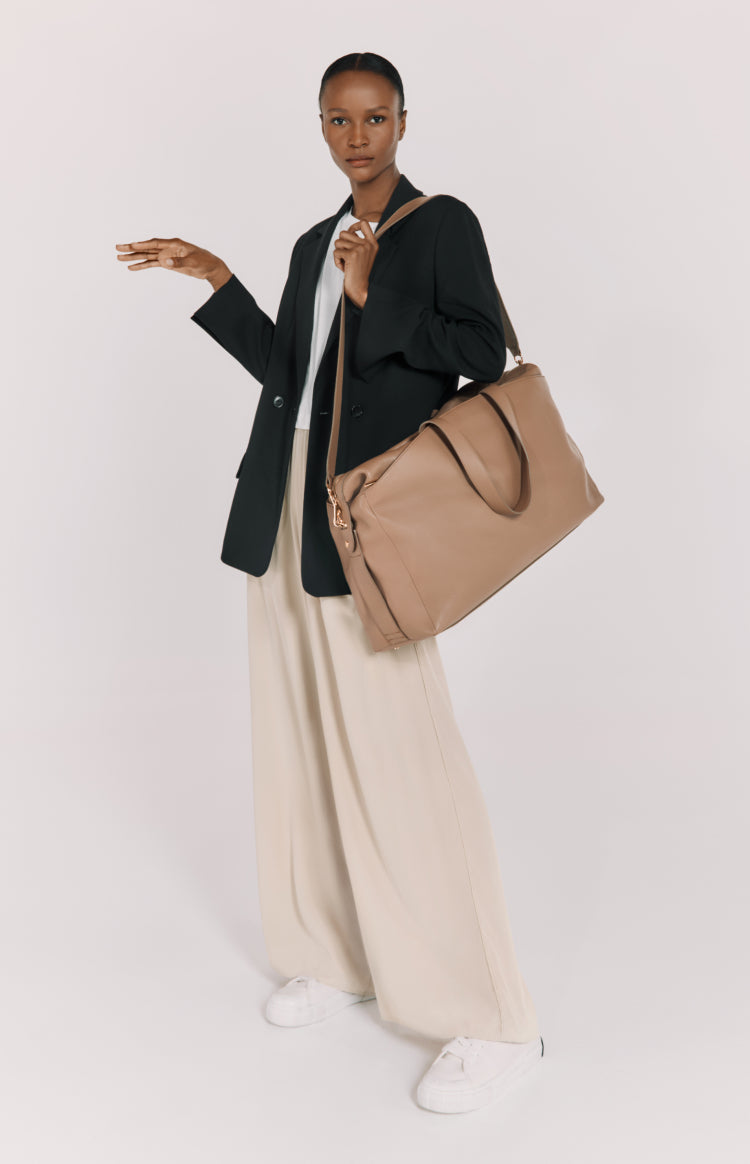 Woman standing with a large bag on her shoulder, gesturing with one hand.