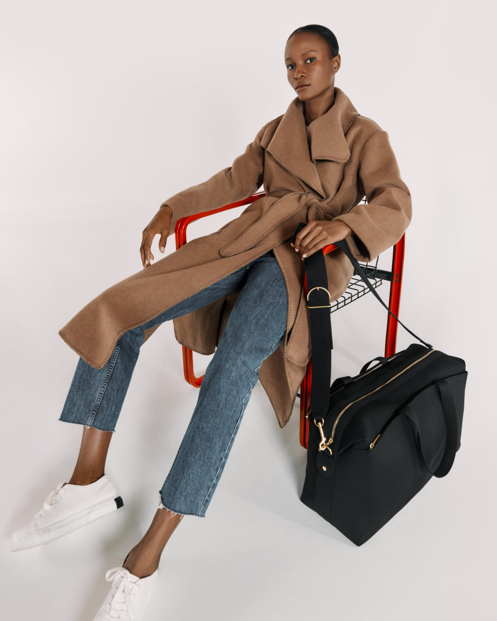 Woman sitting on a red chair with a large bag next to her.