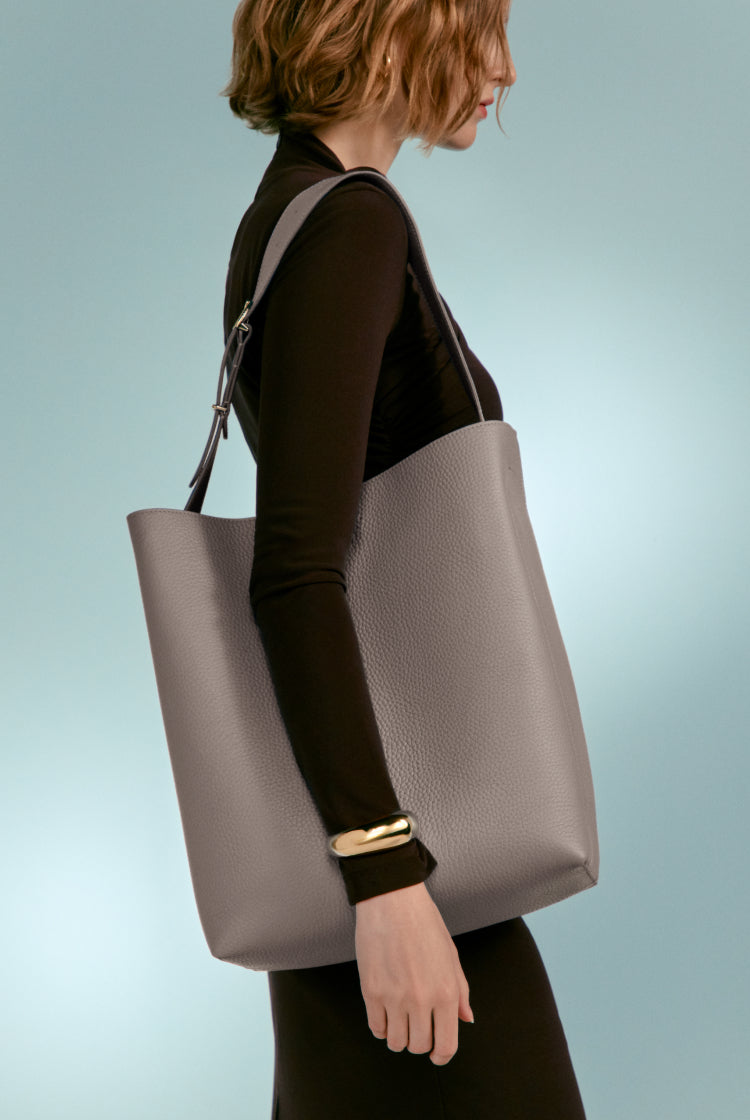 Woman wearing a long sleeve top, carrying a large tote bag.