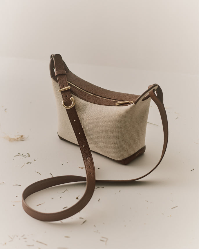 Shoulder bag with long strap on smooth surface with scattered small items around.