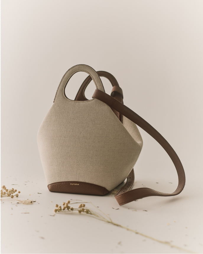 A structured fabric handbag with two handles and a long strap.