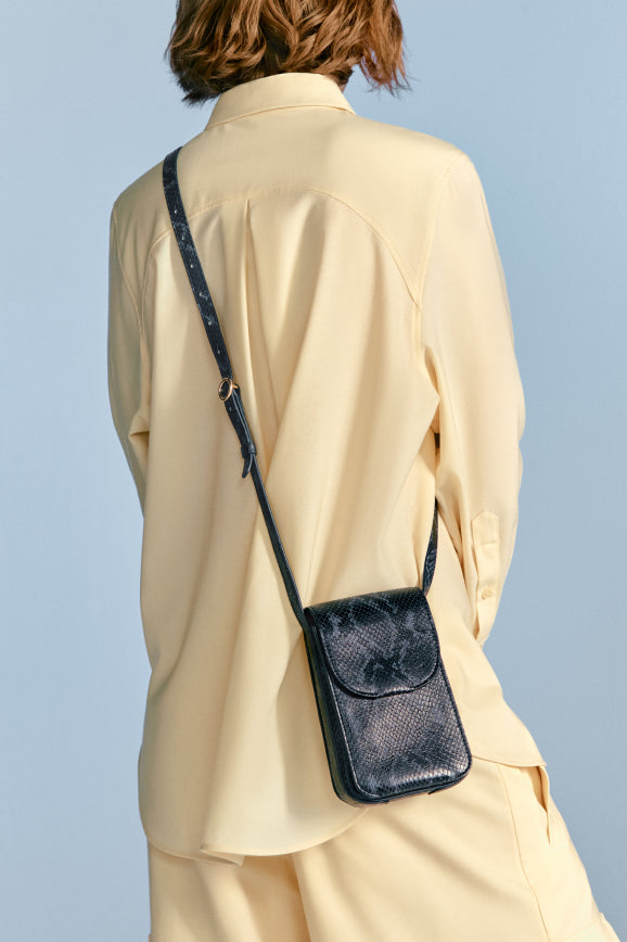 Person wearing a blouse and trousers with a shoulder bag, viewed from behind.