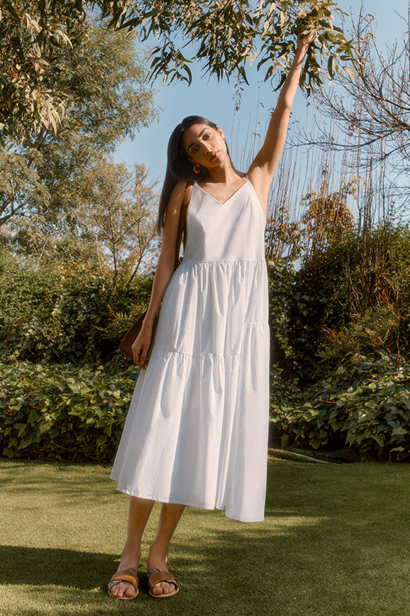 woman in white poplin tiered dress reaching for a tree branch