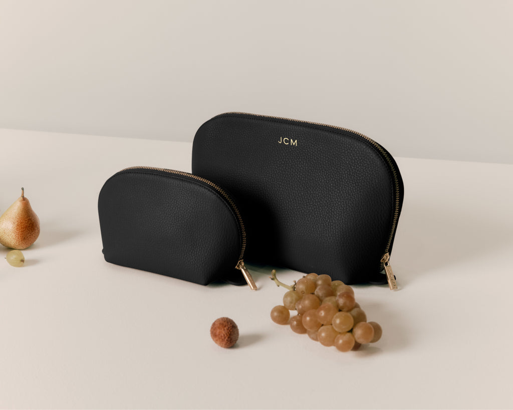 Two cosmetic bags with fruits placed around them.