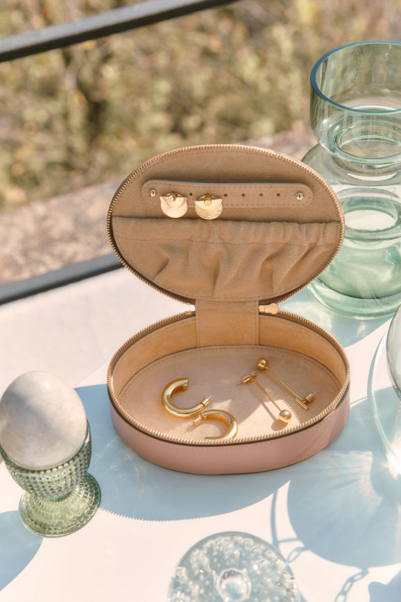 Jewelry case with earrings and pins on a glass table outdoors.